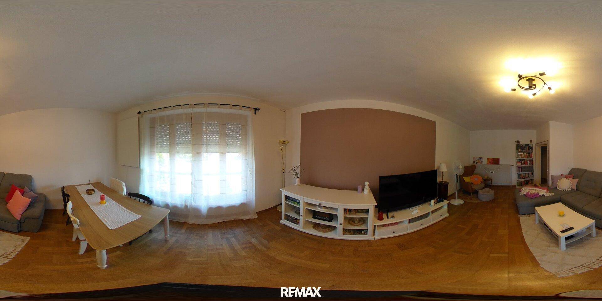 Offener Wohn- und Essbereich mit Holzboden, großem Fenster und gemütlicher Sitzecke.