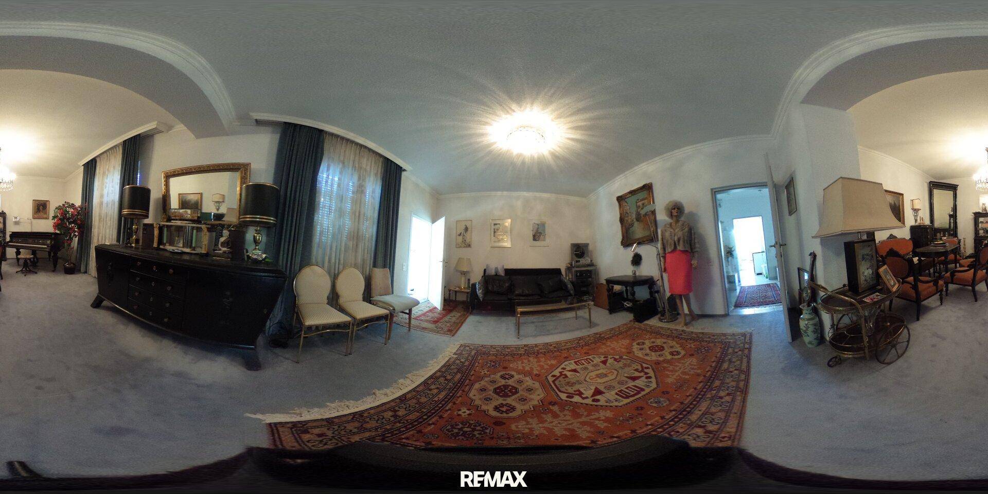 Geräumiges Wohnzimmer mit klassischer Einrichtung, großem Teppich und dunklen Vorhängen.
