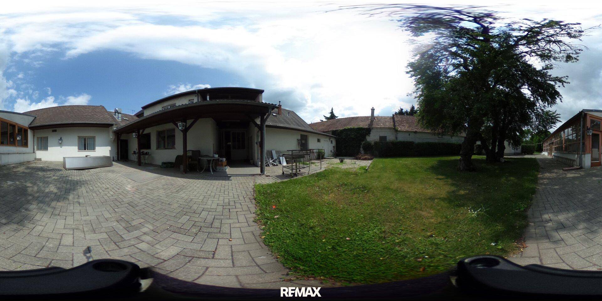 360-Grad-Panorama eines gepflasterten Hofes und einer Rasenfläche mit Gebäuden im Hintergrund.