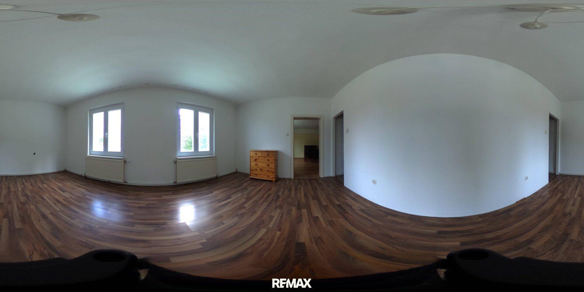 Leerer Raum mit Holzboden, weißen Wänden und zwei Fenstern, die Tageslicht hereinlassen.