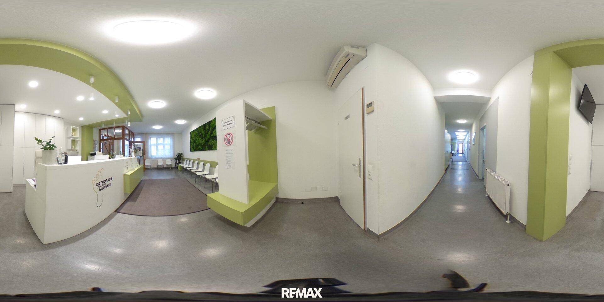 Panoramaansicht des Empfangsbereichs mit Theke, Wartezone und Flur, hell, funktional und klimatisiert.