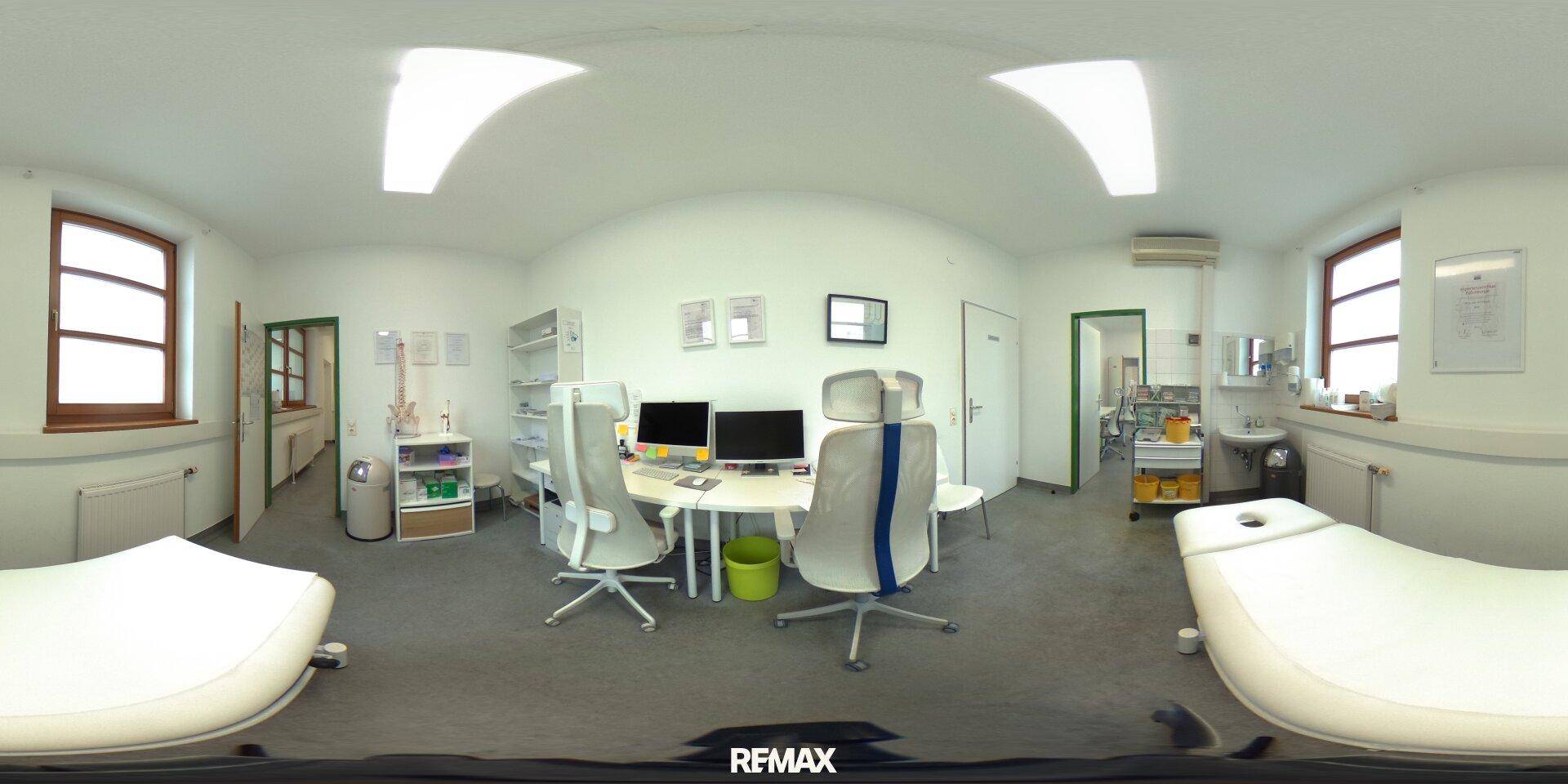 Panoramaansicht eines Untersuchungszimmers mit zwei Schreibtischen, Behandlungsliege und Fenstern, hell und geräumig.