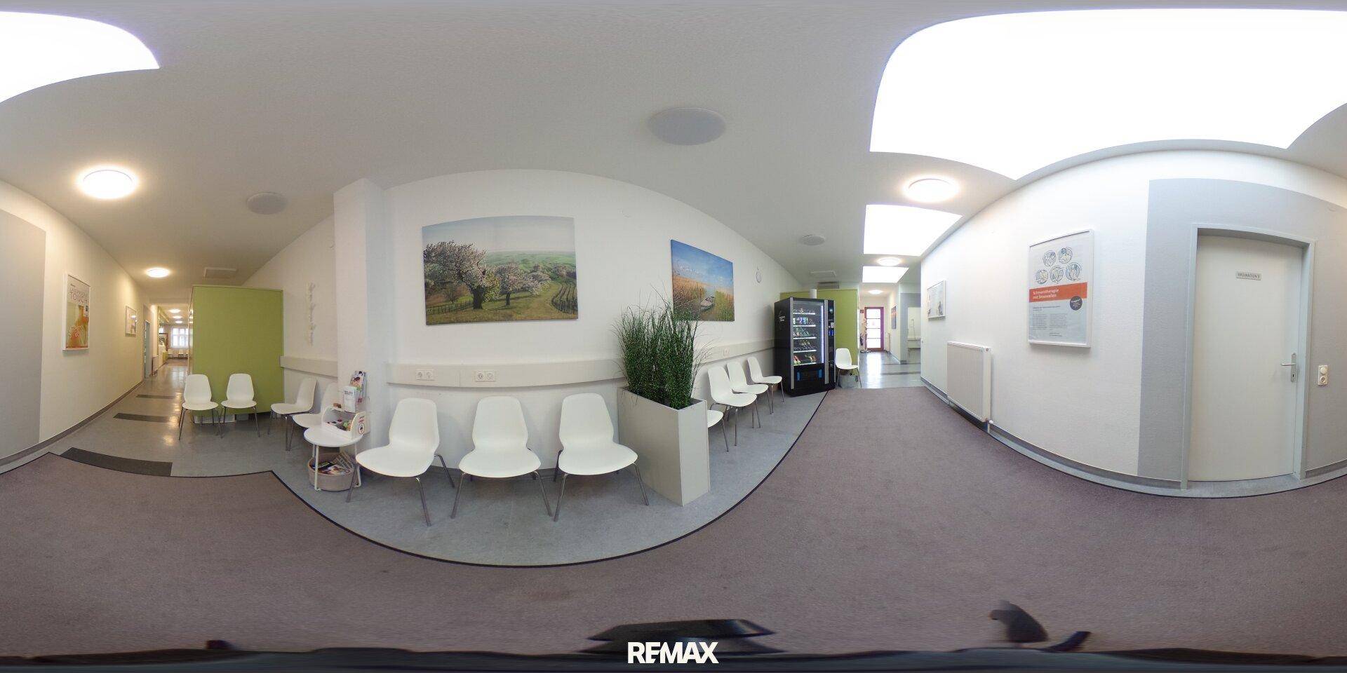 Panoramaansicht des Wartebereichs mit Sitzgelegenheiten, Bildern und einem Verkaufsautomaten, hell und modern.