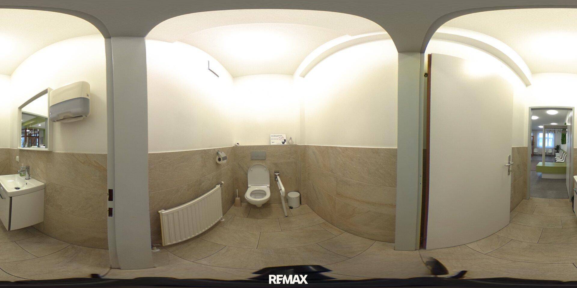 Panoramaansicht einer Toilette mit Waschbecken, Spiegel und beigefarbenen Fliesen, sauber und funktional gestaltet.
