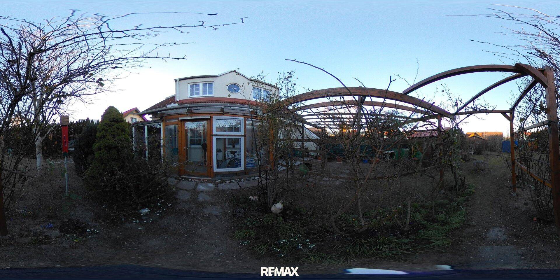 Großer Gartenbereich mit Holzpergola, Sträuchern und Blick auf das Haus.