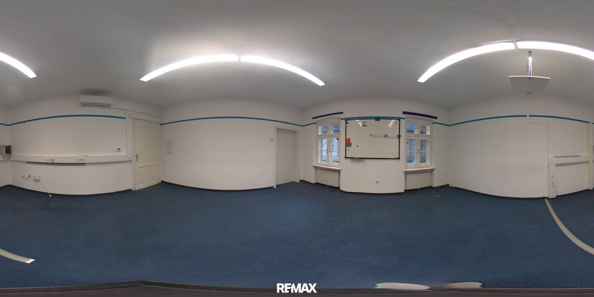 Panoramablick auf ein geräumiges Büro mit blauem Teppichboden, weißen Wänden und Leuchtstoffröhren.