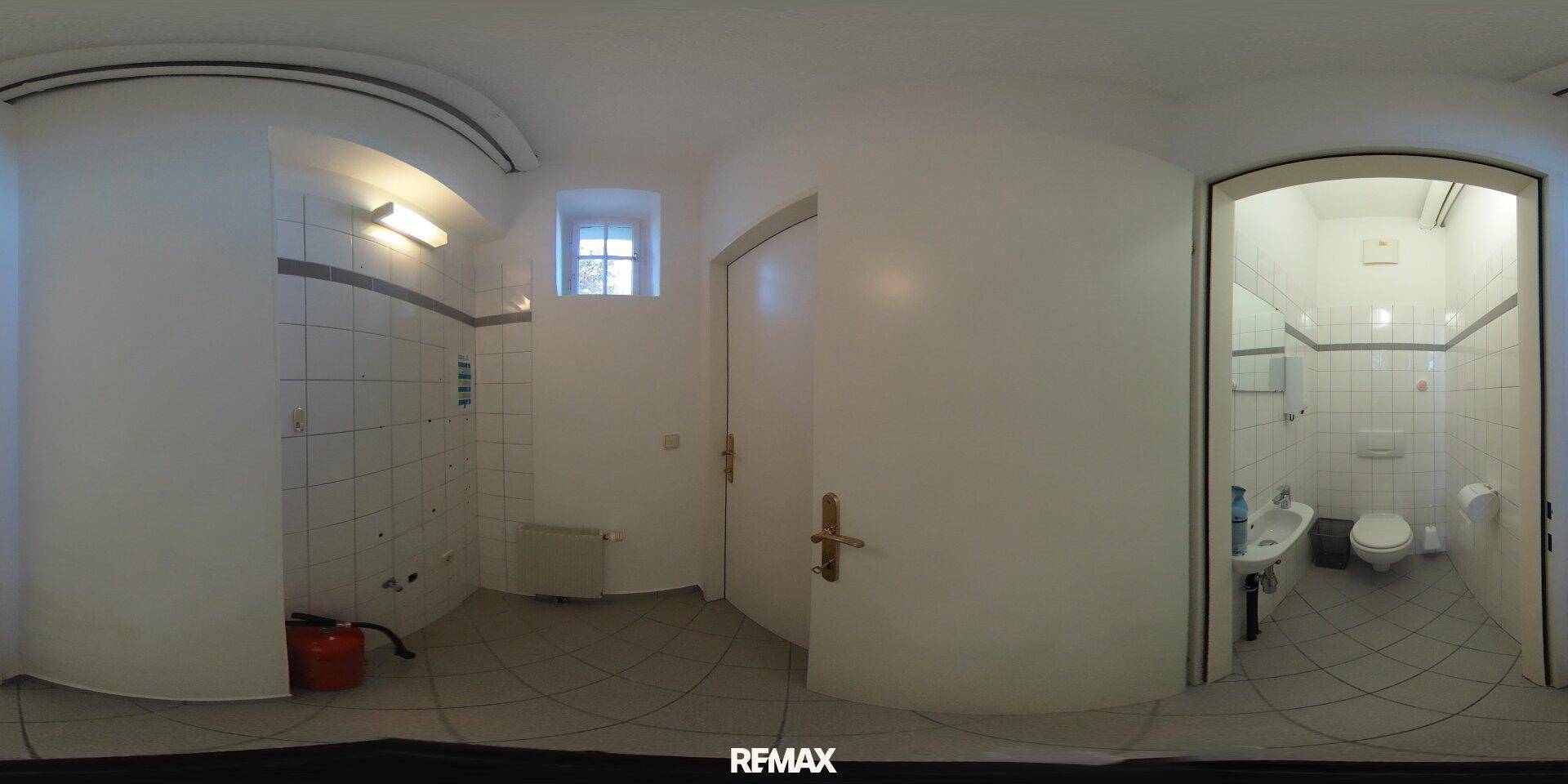 Panoramablick auf einen Flur mit Zugang zu einem gefliesten Badezimmer und einem kleinen Fenster.