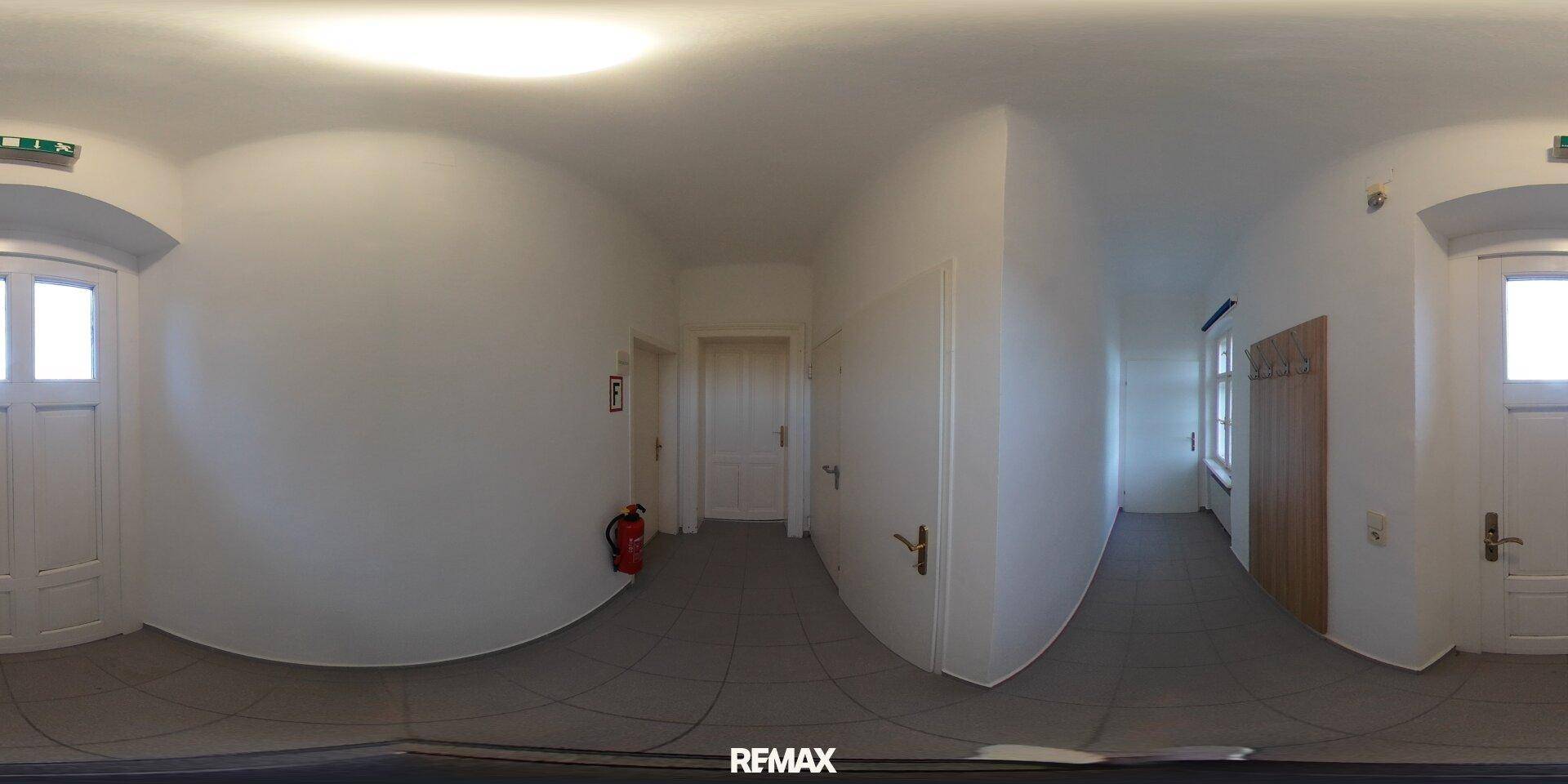 Panoramablick auf einen hellen Flur mit weißen Wänden, grauen Fliesen und mehreren Türen.