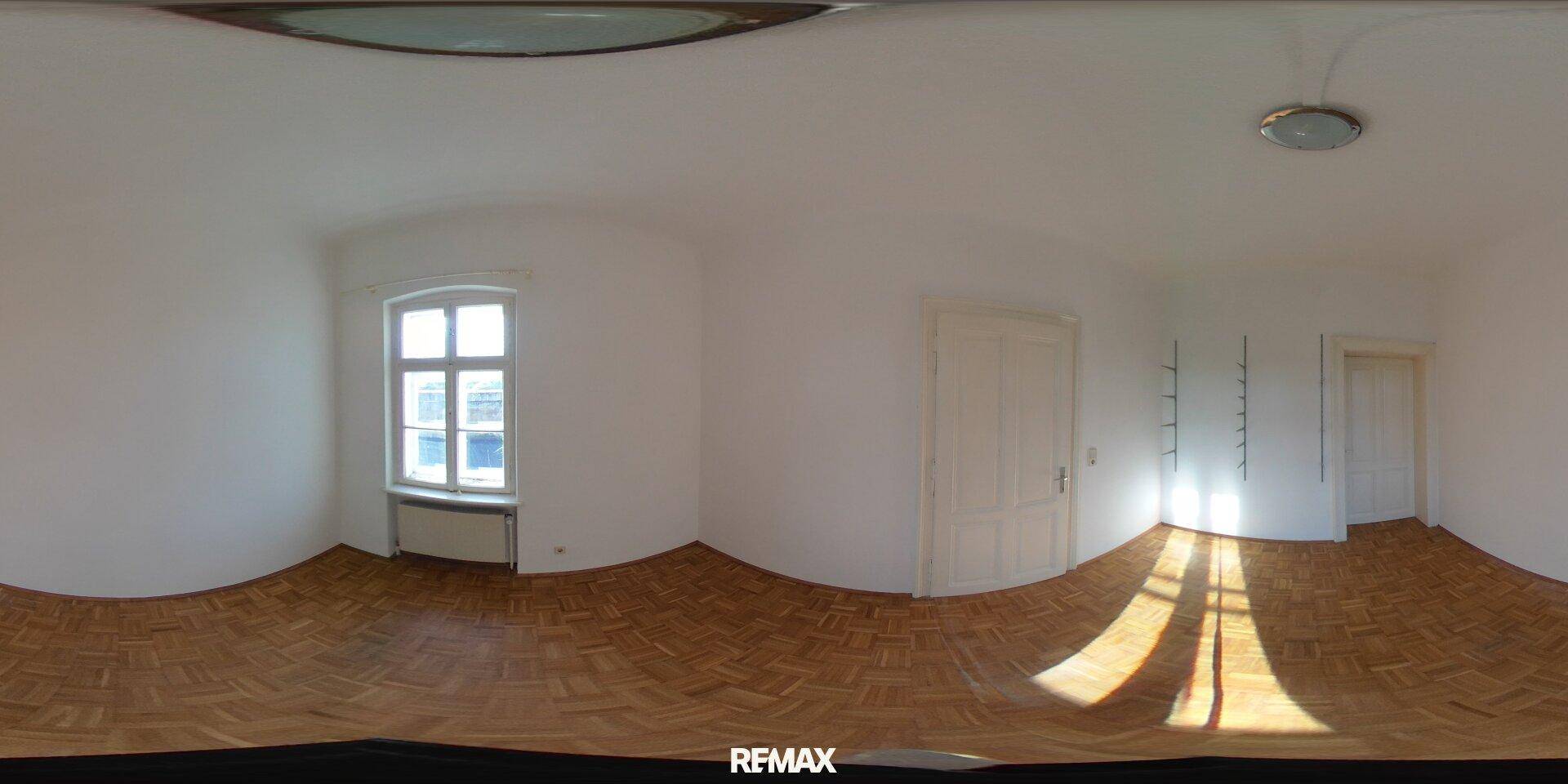 Panorama eines hellen Raumes mit Parkettboden, einem Fenster und weißen Wänden.
