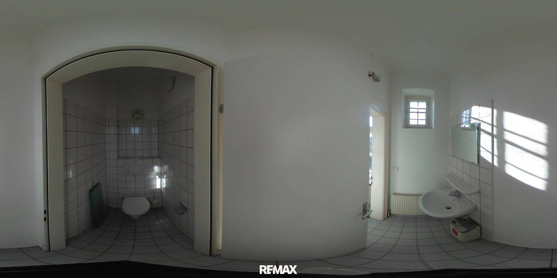 Panorama des Badezimmers mit weißen Fliesen, WC und Waschbeckenbereich.