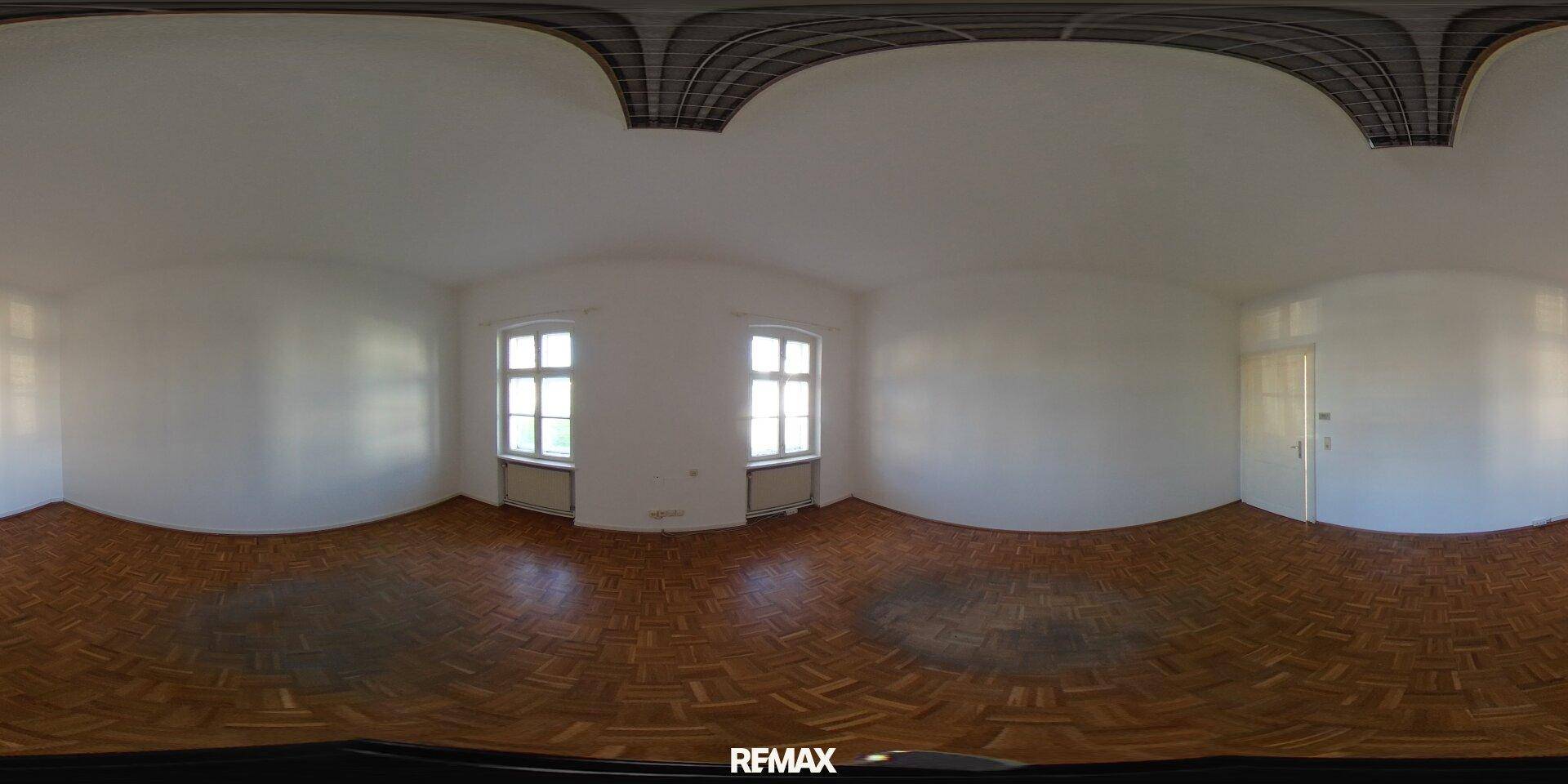 Panorama eines geräumigen Zimmers mit Parkettboden, zwei Fenstern und weißen Wänden.