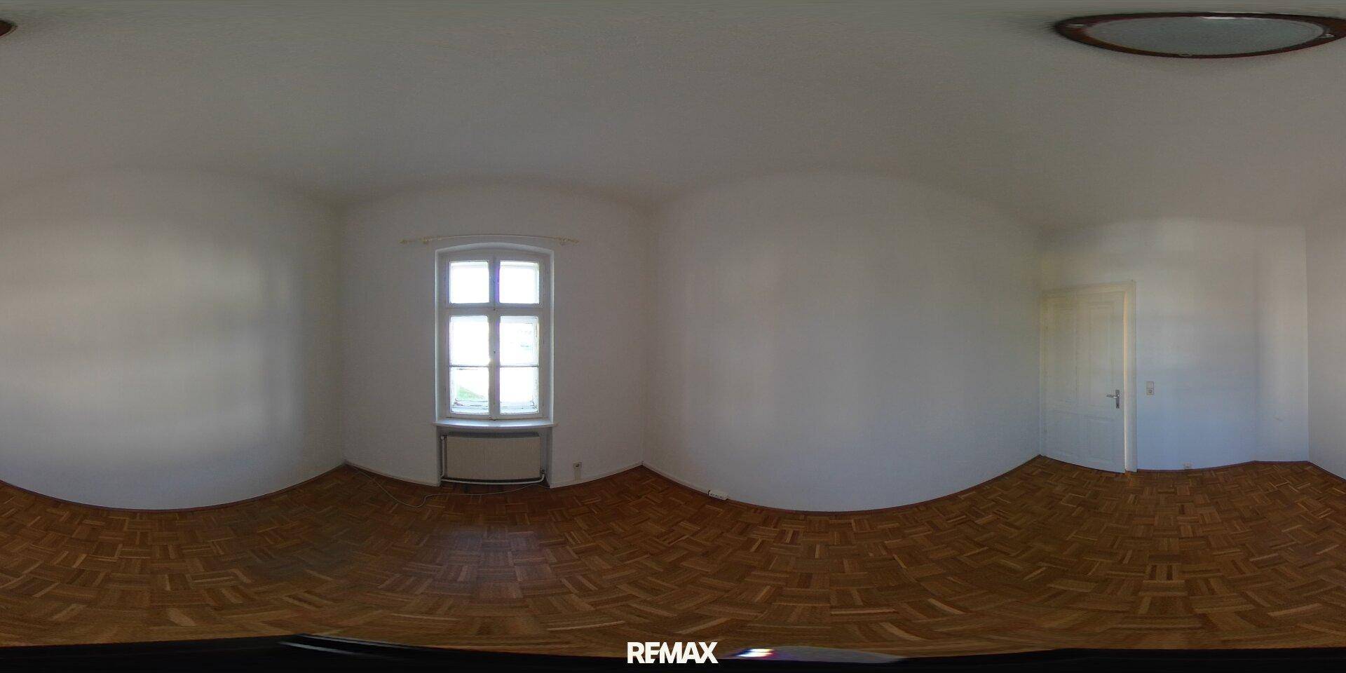 Panorama eines leeren Raumes mit Parkettboden, einem Fenster und viel Tageslicht.