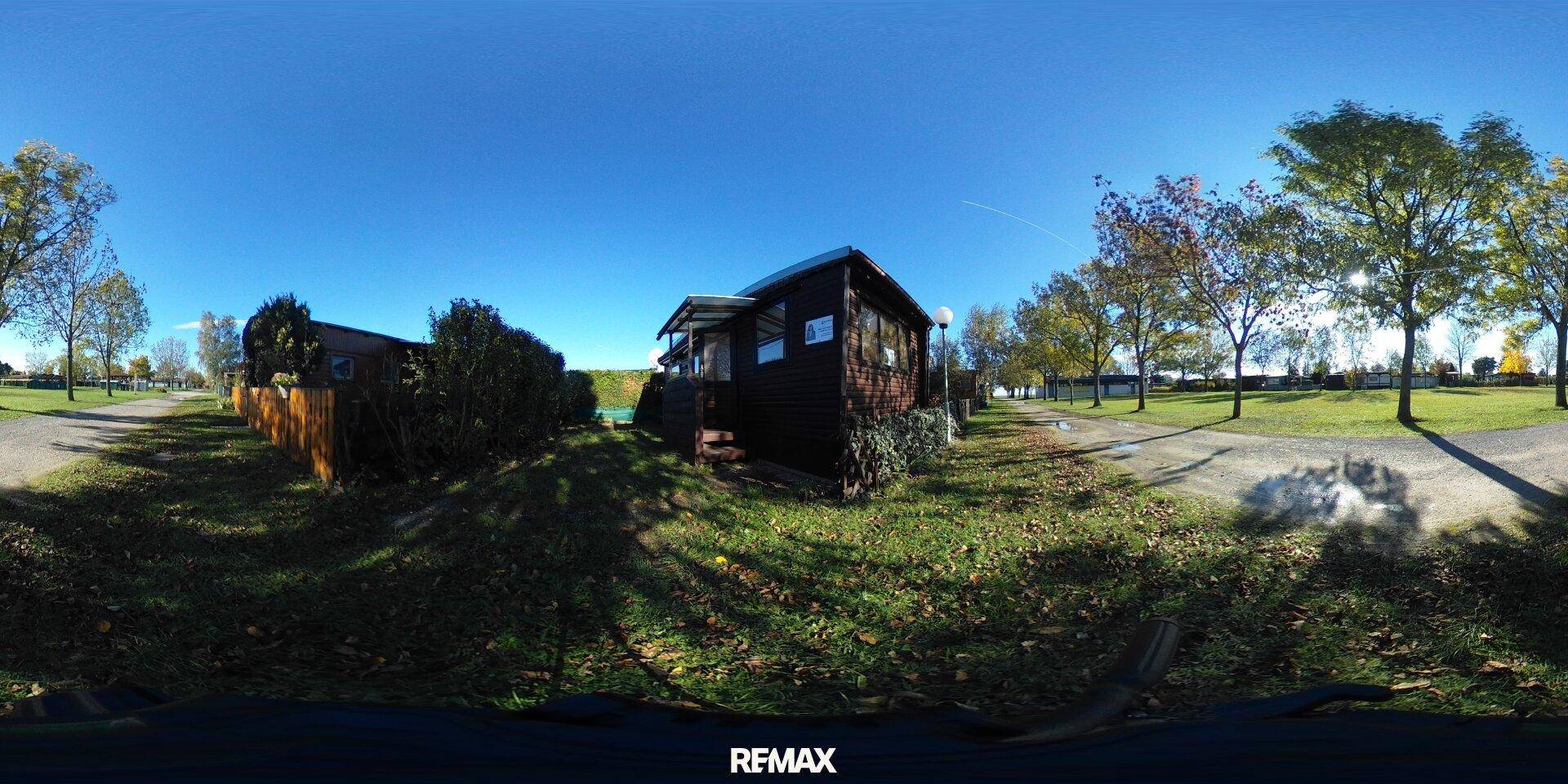 Panoramablick auf das Holzhaus und die grüne Umgebung unter klarem blauem Himmel.