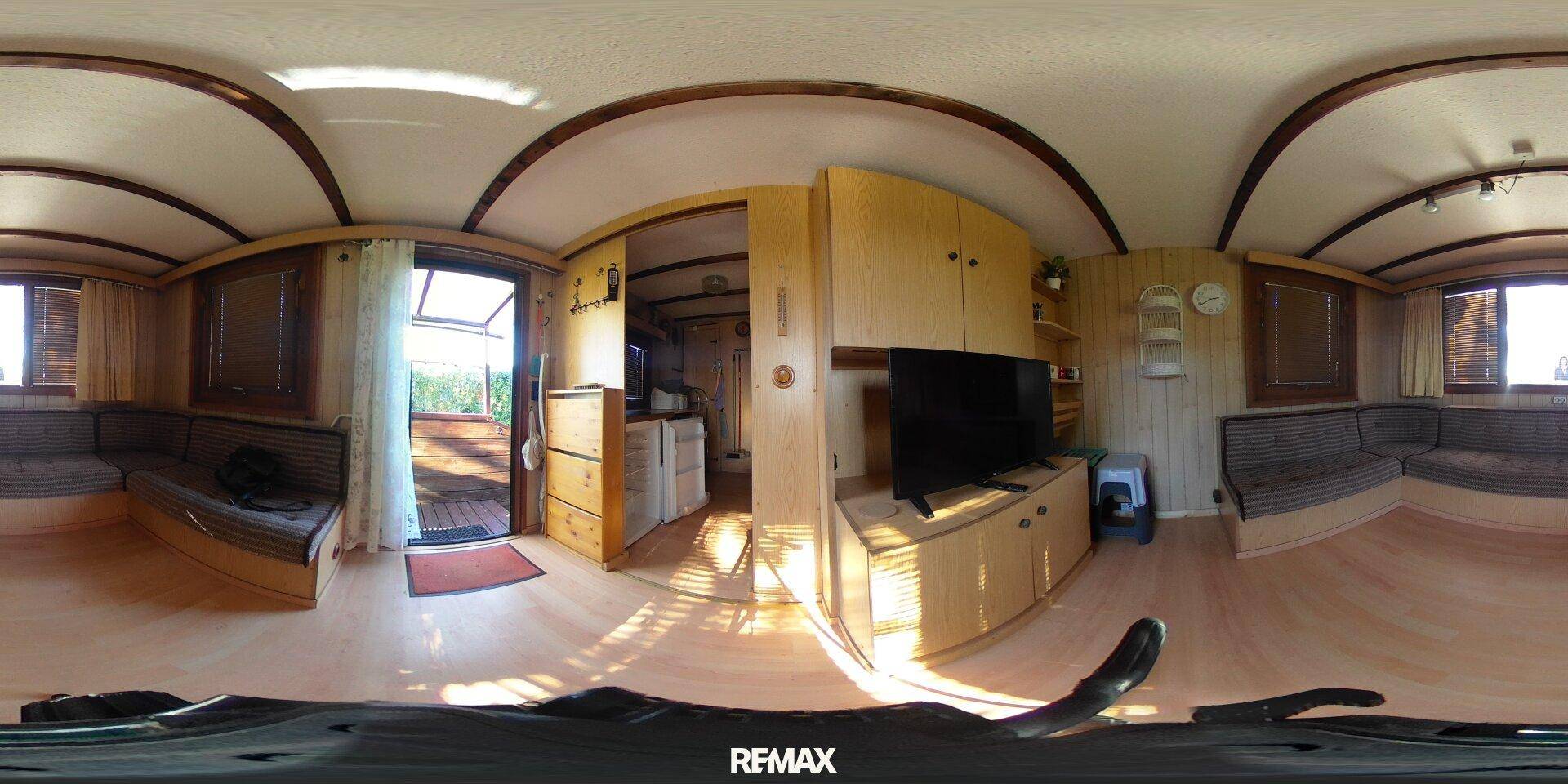 Panoramablick auf den Wohnbereich mit gewölbter Decke, Sitzgelegenheiten und Fernseher.