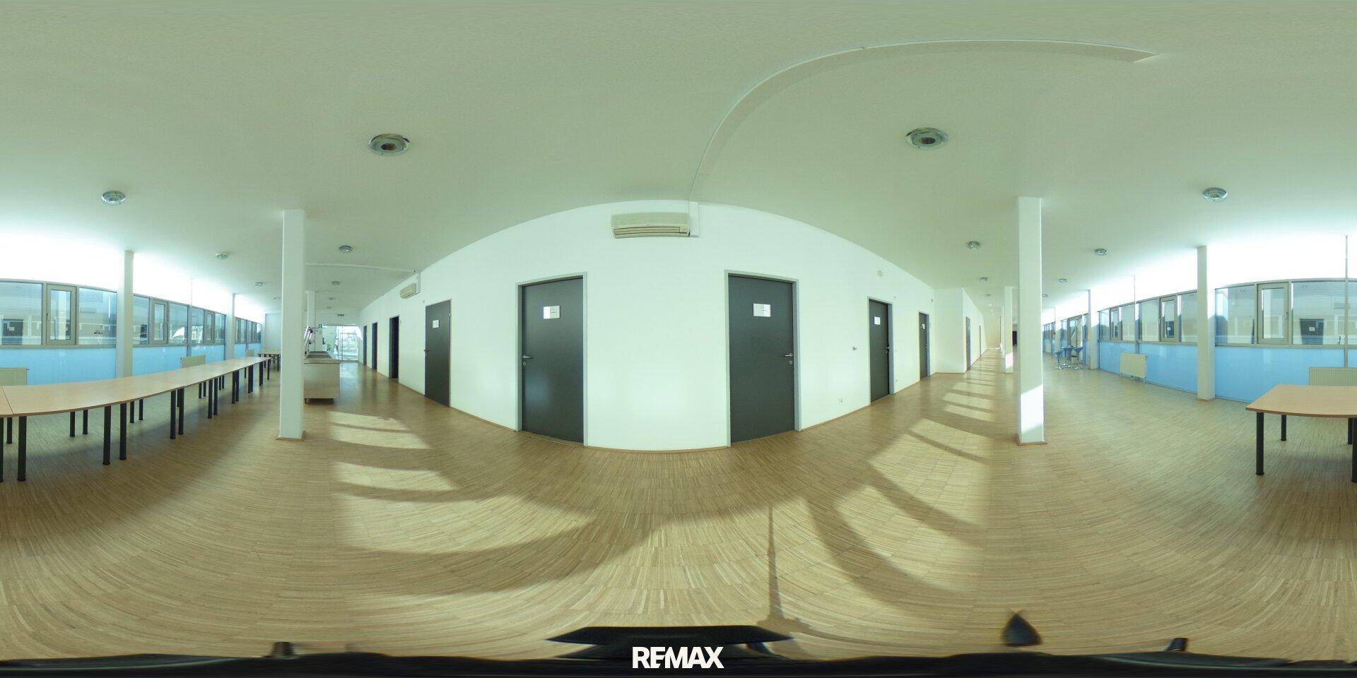 Heller Großraumbüro-Bereich mit Holzfußboden und vielen Fenstern, ideal für flexible Arbeitsplätze.