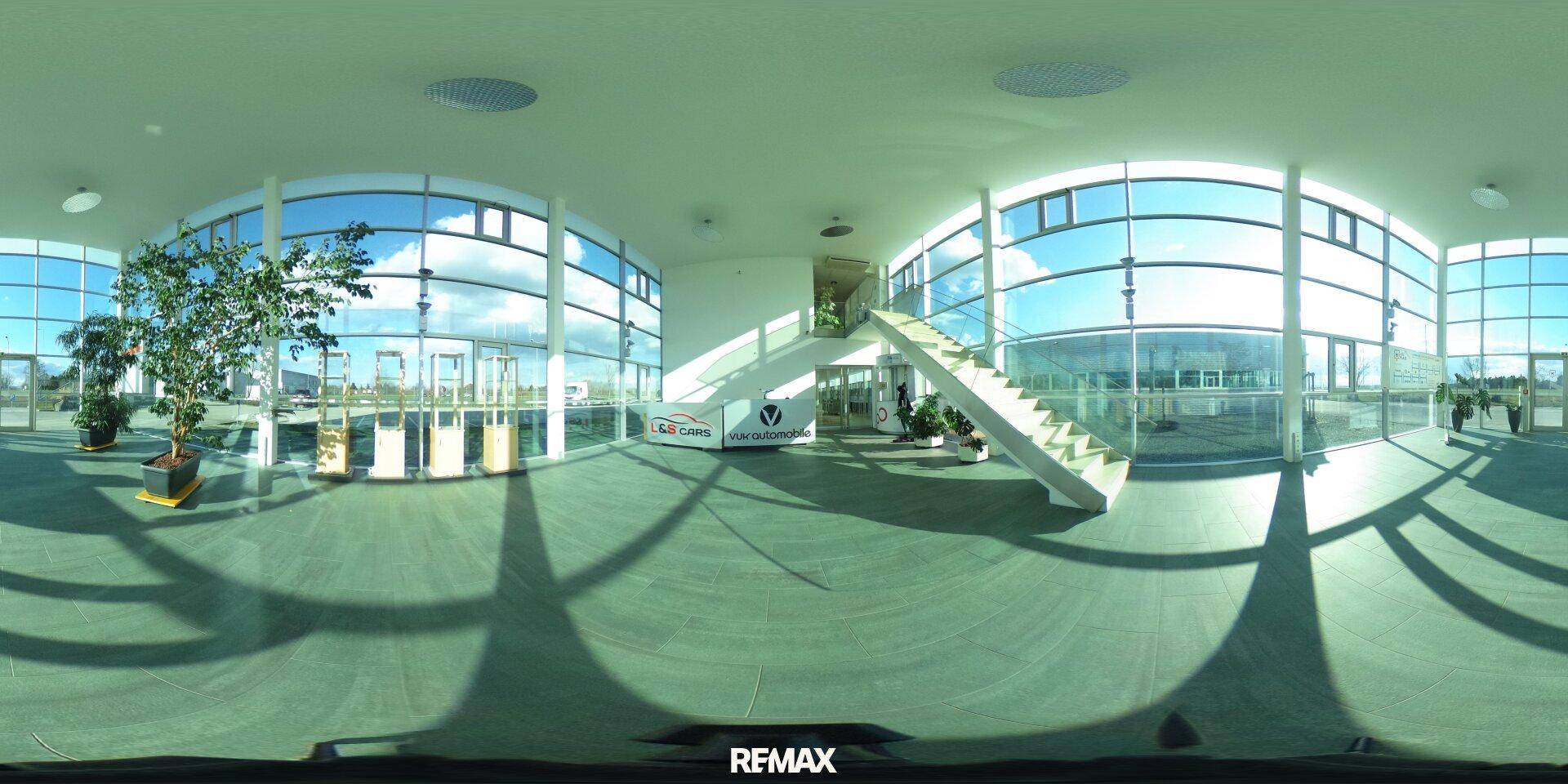Moderne Lobby mit großer Glasfassade, viel Tageslicht und einer eleganten Treppe.