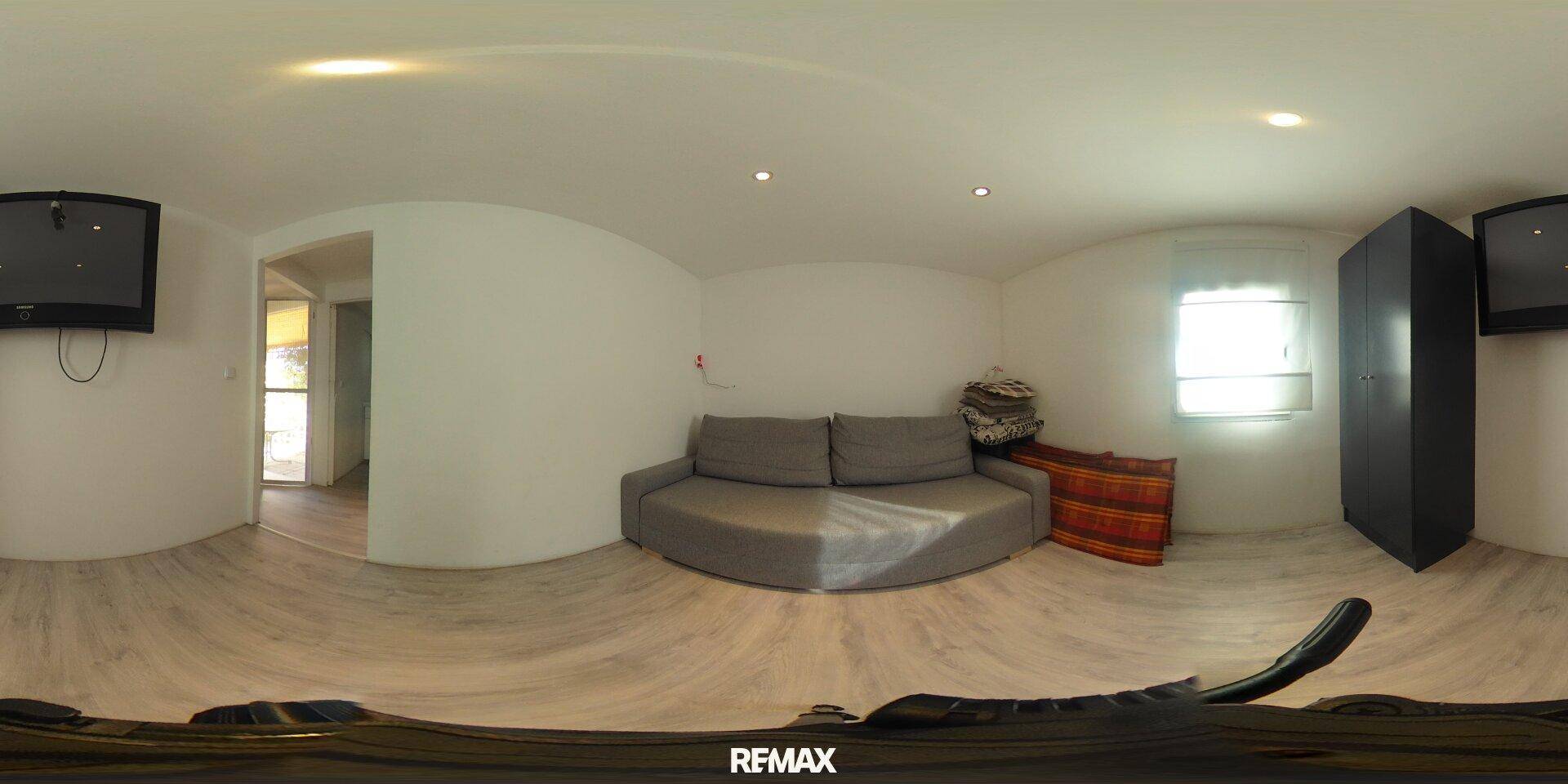 Gemütliches Wohnzimmer mit grauem Sofa, hellem Laminatboden und Fenster in einer 360-Grad-Ansicht.