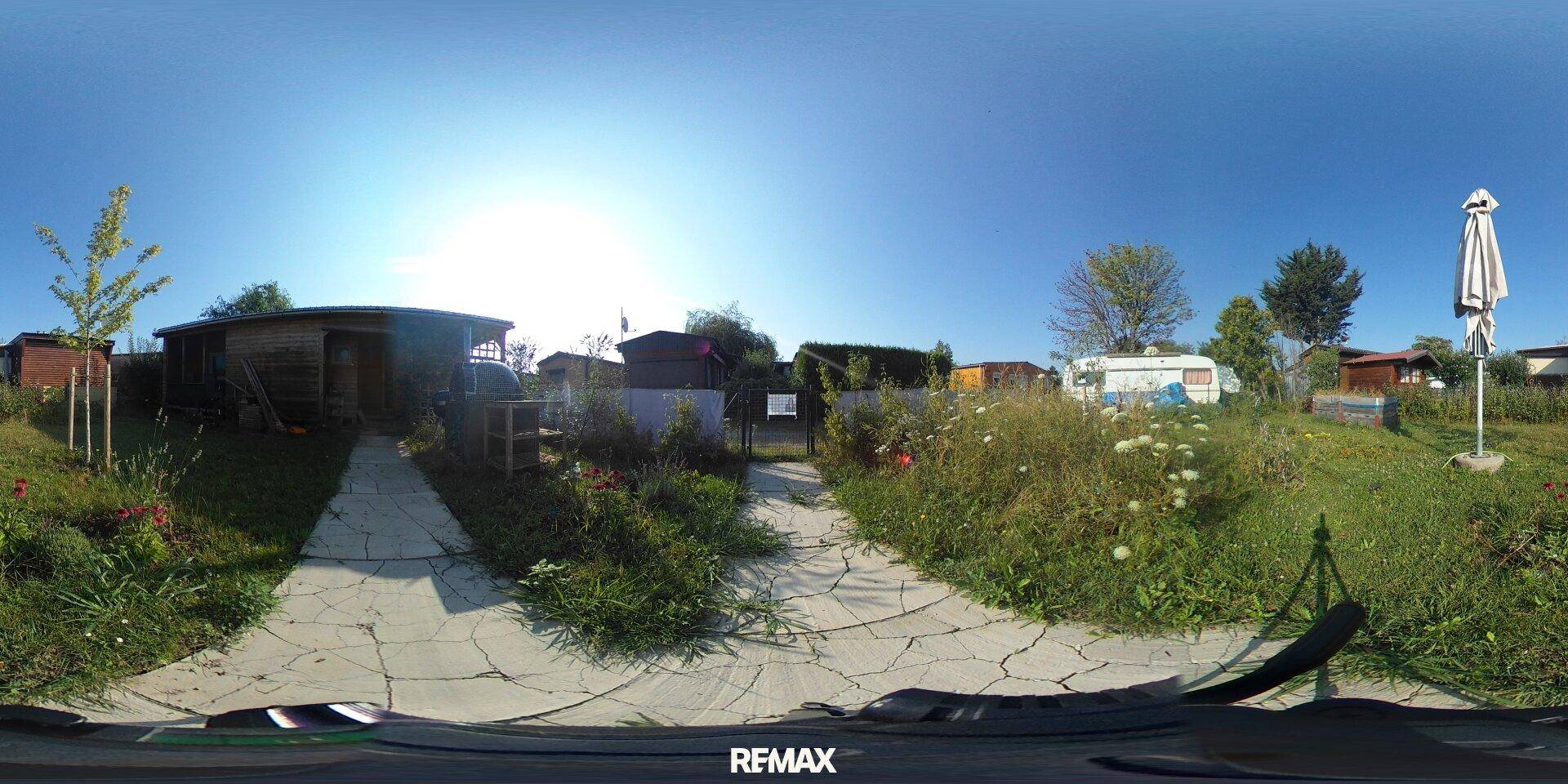 Weitläufiger Gartenbereich mit gepflastertem Weg, viel Grün und Sonnenschirm unter blauem Himmel.