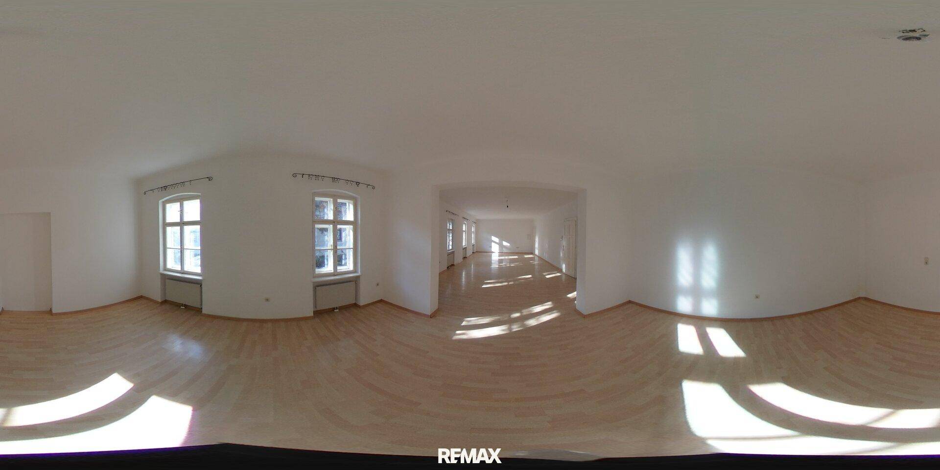 360-Grad-Innenansicht eines weitläufigen, leeren Raumes mit hellem Laminatboden und mehreren Fenstern.