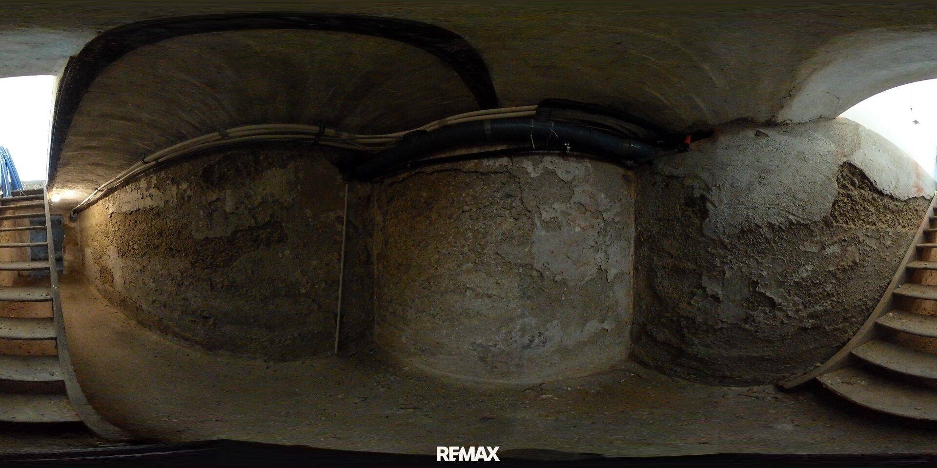 Alter Kellerraum mit rauen Steinwänden, sichtbaren Rohren und Betondecke.