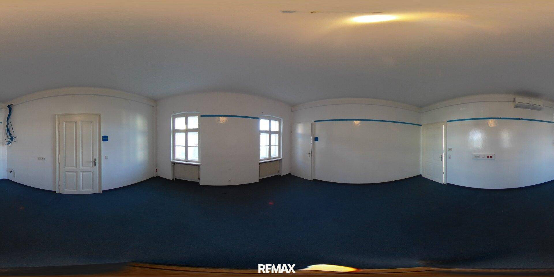 Großer Raum mit dunklem Teppichboden, zwei Fenstern und mehreren Türen.