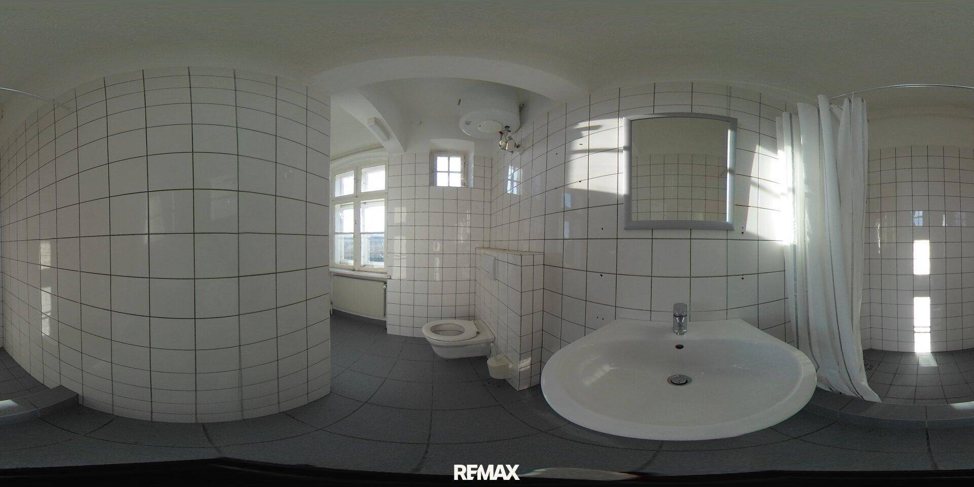 Gefliestes Badezimmer mit Waschbecken, Toilette, Duschbereich und Fenster.