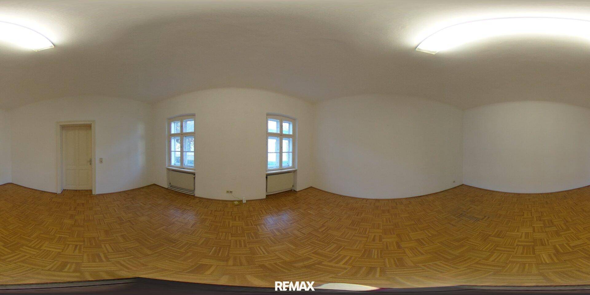 Helles, leeres Zimmer mit Parkettboden und weißen Wänden, das viel natürliches Licht durch die Fenster erhält.