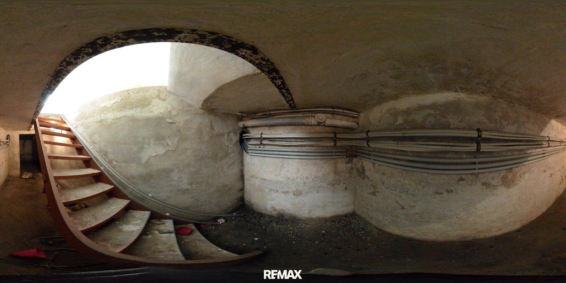 Kellerbereich mit einer Holztreppe, rauen Betonwänden und sichtbaren Leitungen, die eine industrielle Ästhetik verleihen.