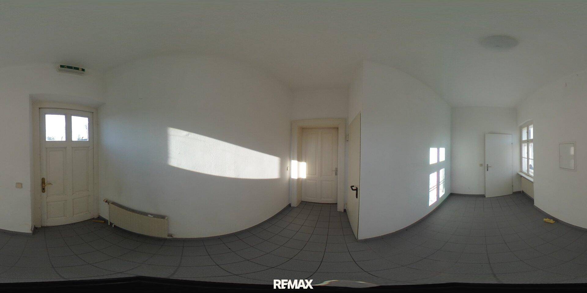 Leerer Innenraum mit Fliesenboden und weißen Wänden, durch ein Fenster fällt Sonnenlicht herein.