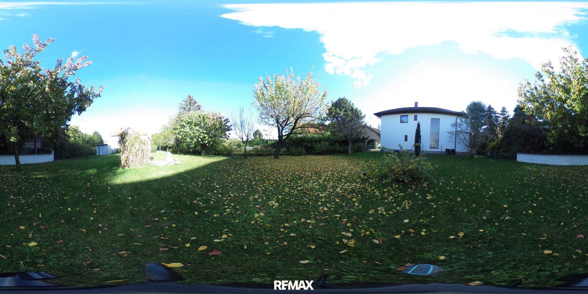 Weitläufiger Gartenbereich mit Rasenfläche, Bäumen und einem Einfamilienhaus im Hintergrund.
