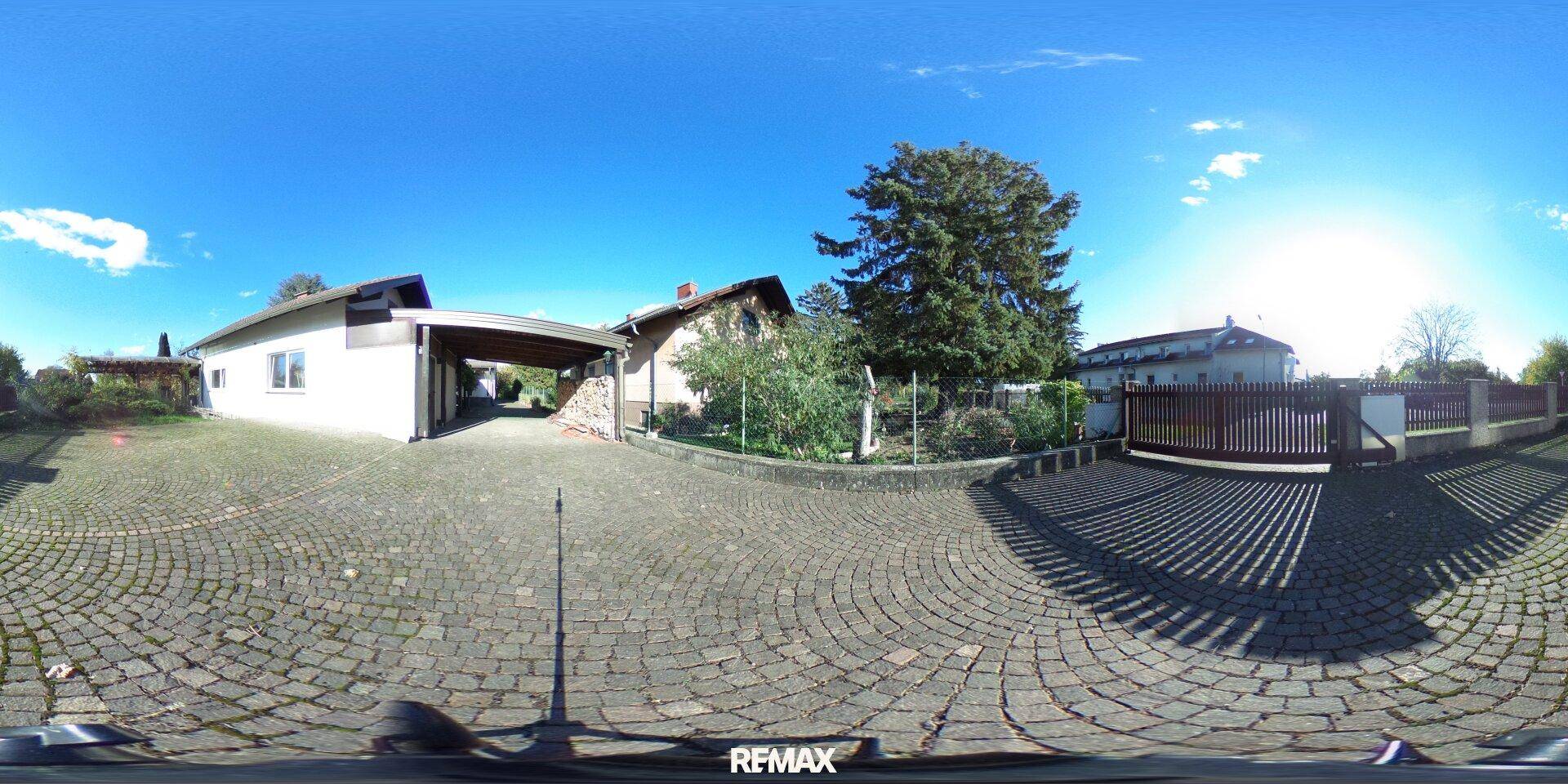 Außenansicht des Hauses mit gepflasterter Auffahrt, Carport und altem Baumbestand.