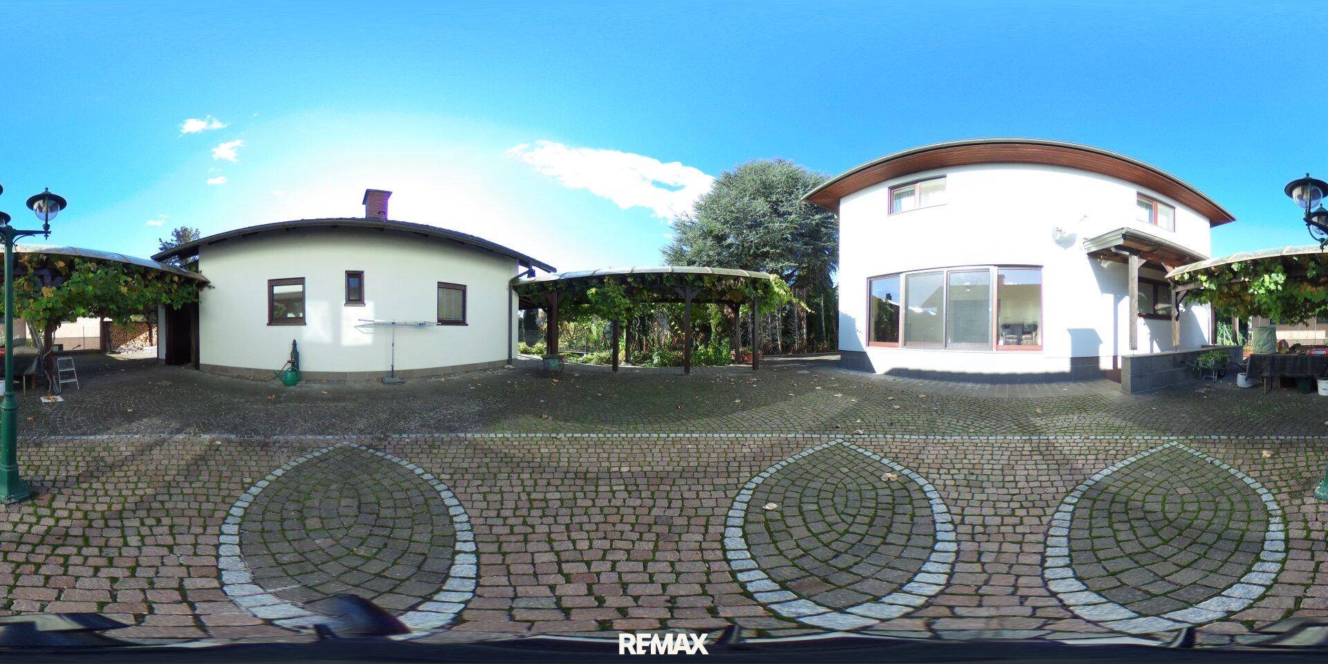 Gepflasterter Innenhof zwischen zwei Gebäuden mit einer begrünten Pergola.