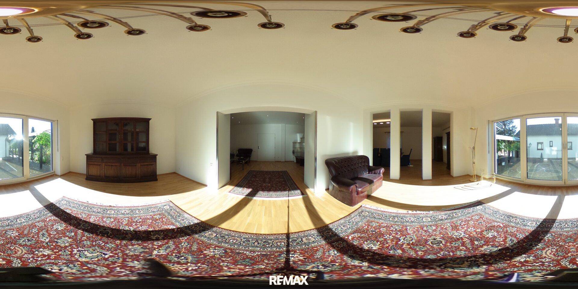 Geräumiges Wohnzimmer mit traditionellen Möbeln, gemustertem Teppich und großen Fenstern mit Blick ins Grüne.