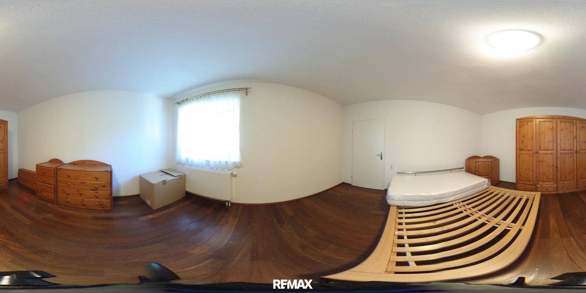 Schlafzimmer mit Holzboden, einfachem Bettgestell und Kommoden, hell durch ein Fenster.