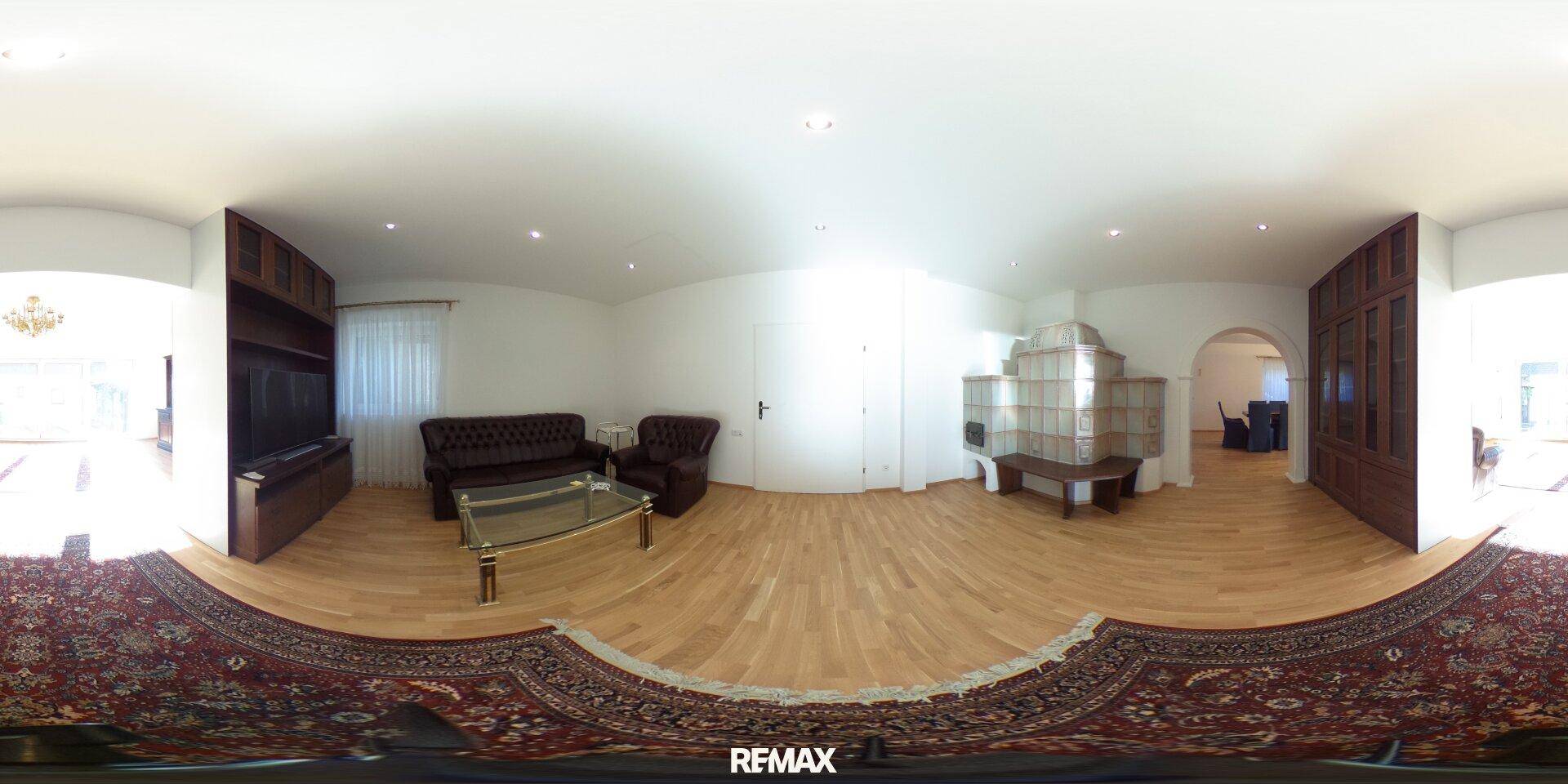 Helles Wohnzimmer mit Kachelofen, Holzboden und traditionellem Sofa.