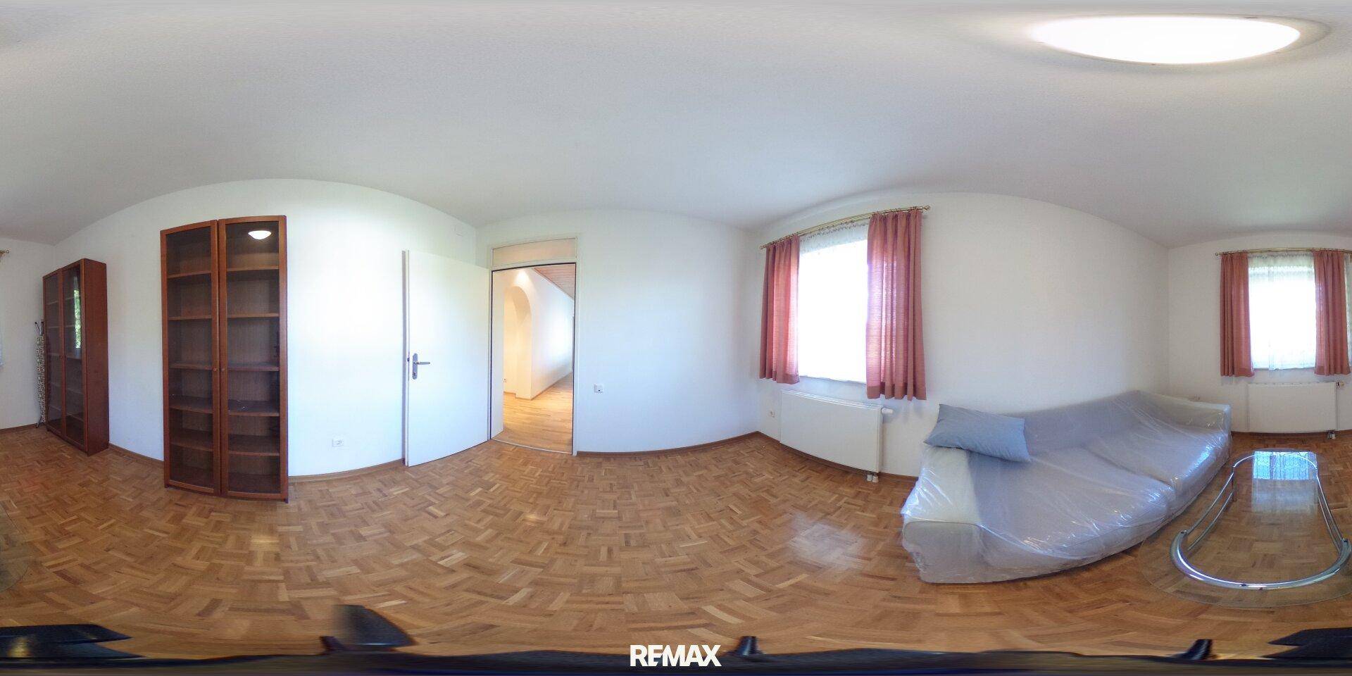 Heller Raum mit Parkettboden, einem Sofa und einem Holzregal, mit Blick nach draußen.