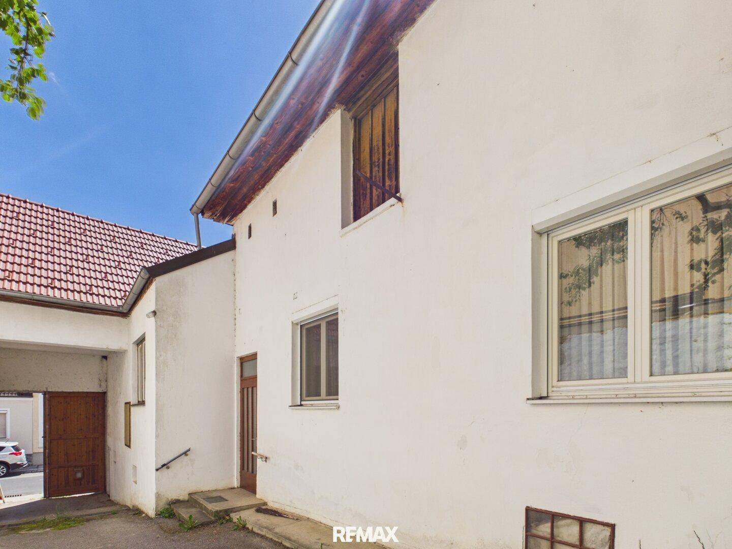 Weißes Gebäude mit rotem Ziegeldach, Torbogen und einfachem Eingangsbereich.