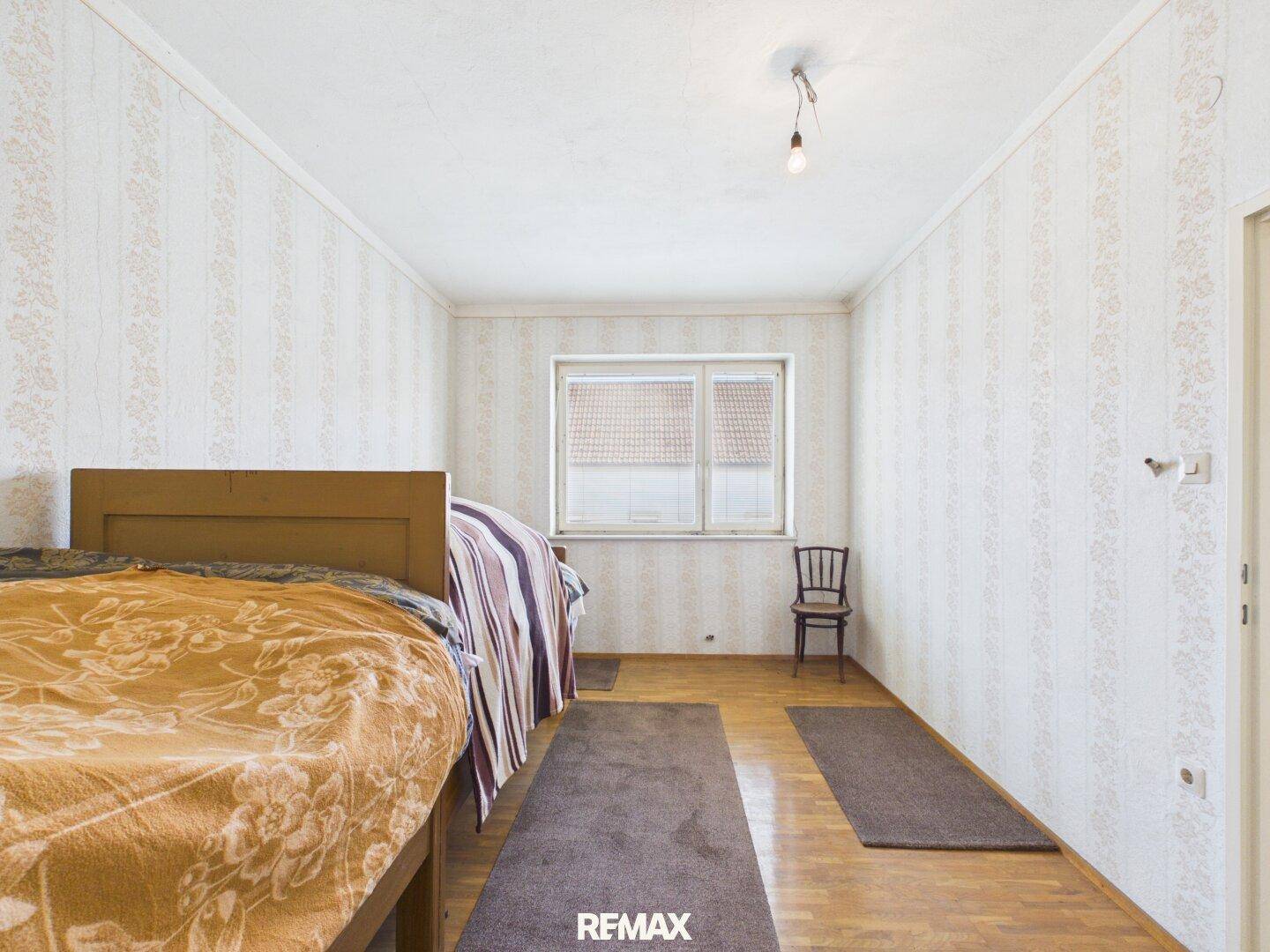 Schlafzimmer mit gemusterter Tapete, Holzboden und einem großen Fenster.