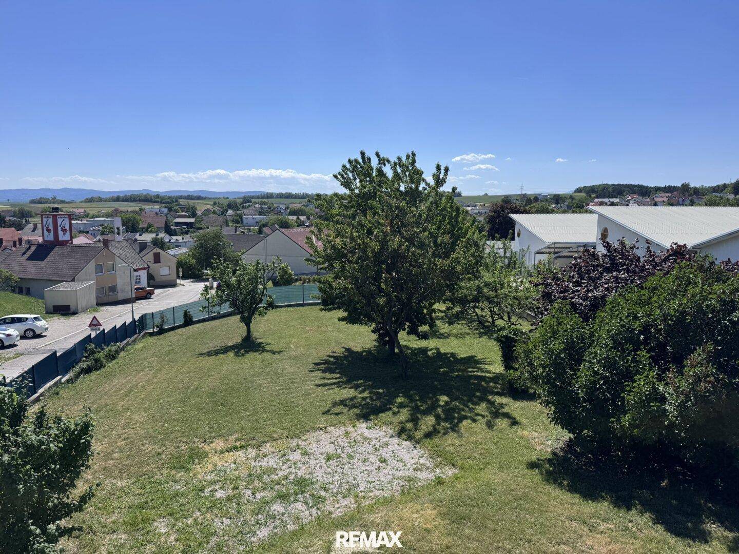 Weitläufiger Garten mit Rasenfläche und Blick auf die umliegende Landschaft und Siedlung.