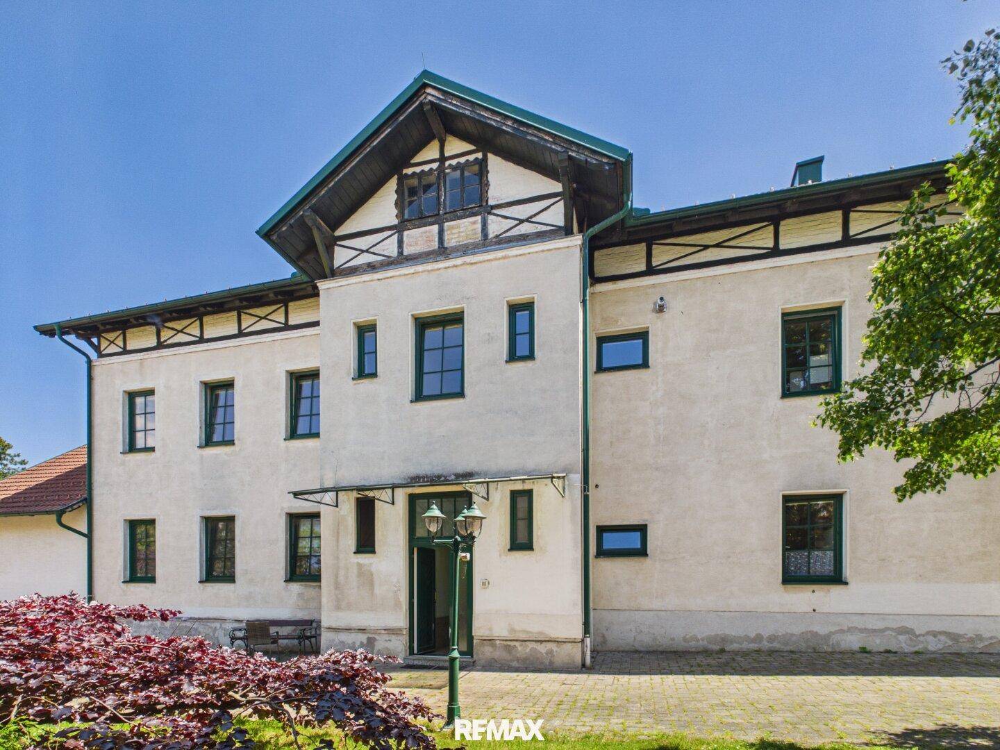 Repräsentative Fassade eines historischen Gebäudes mit grünen Fensterrahmen und einem Vordach über dem Eingang.