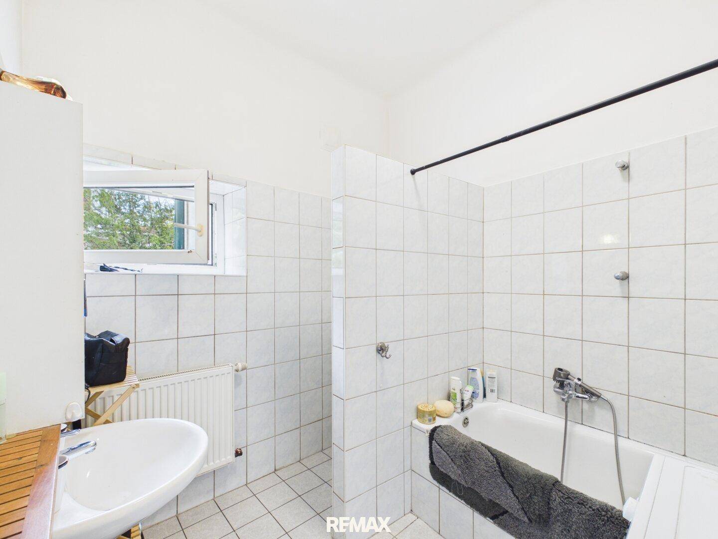 Gefliestes Badezimmer mit Badewanne, Waschbecken und einem Fenster für Tageslicht.