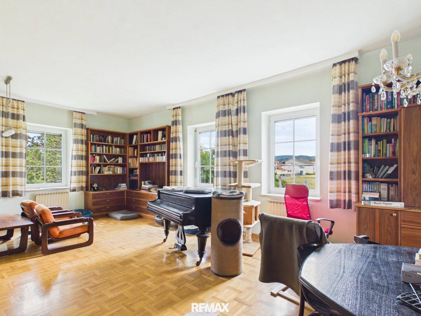 Großes Wohnzimmer mit Parkettboden, Bücherregalen, einem Flügel und Blick auf die Umgebung.