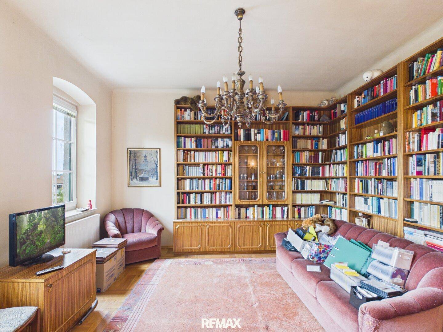 Gemütliche Bibliothek mit raumhohen Bücherregalen, Sofa und einem Fenster für natürliches Licht.