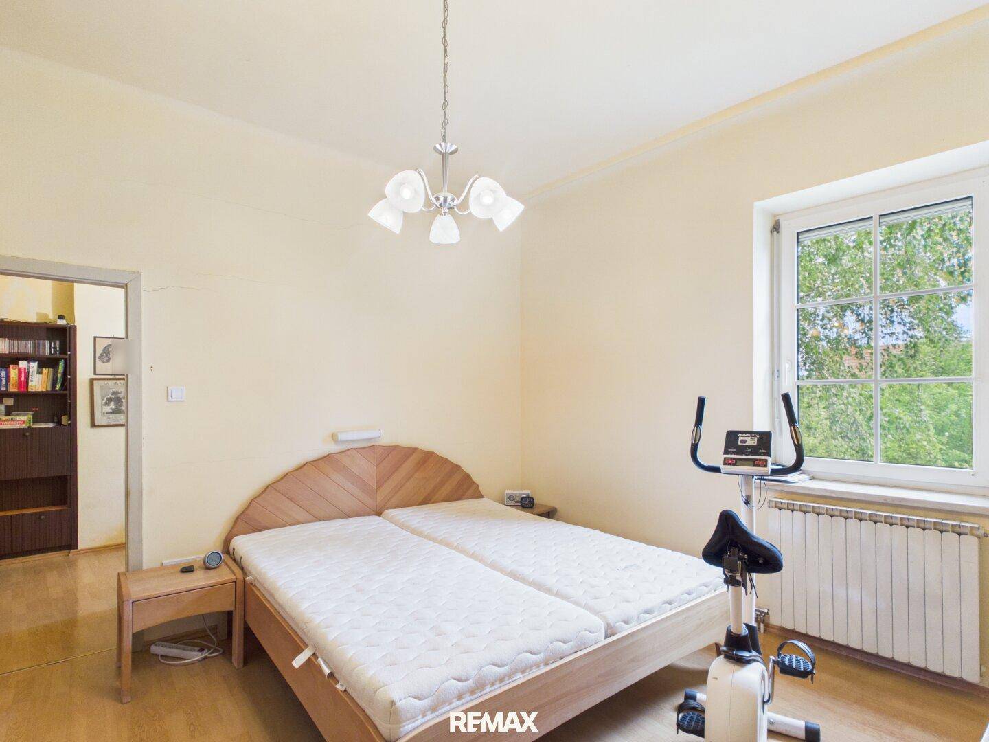 Geräumiges Schlafzimmer mit Holzbett, Parkettboden und einem Fenster, das viel Licht hereinlässt.