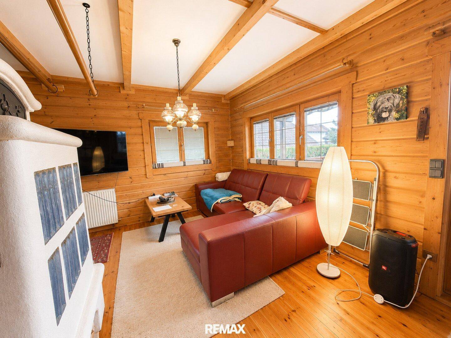 Helles Wohnzimmer mit Holzbalkendecke, Kachelofen und bequemer Ledercouch.