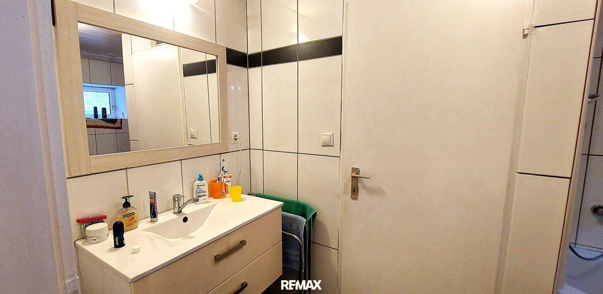 Badezimmer mit weiß gefliesten Wänden, Einzelwaschbecken und Spiegelschrank.