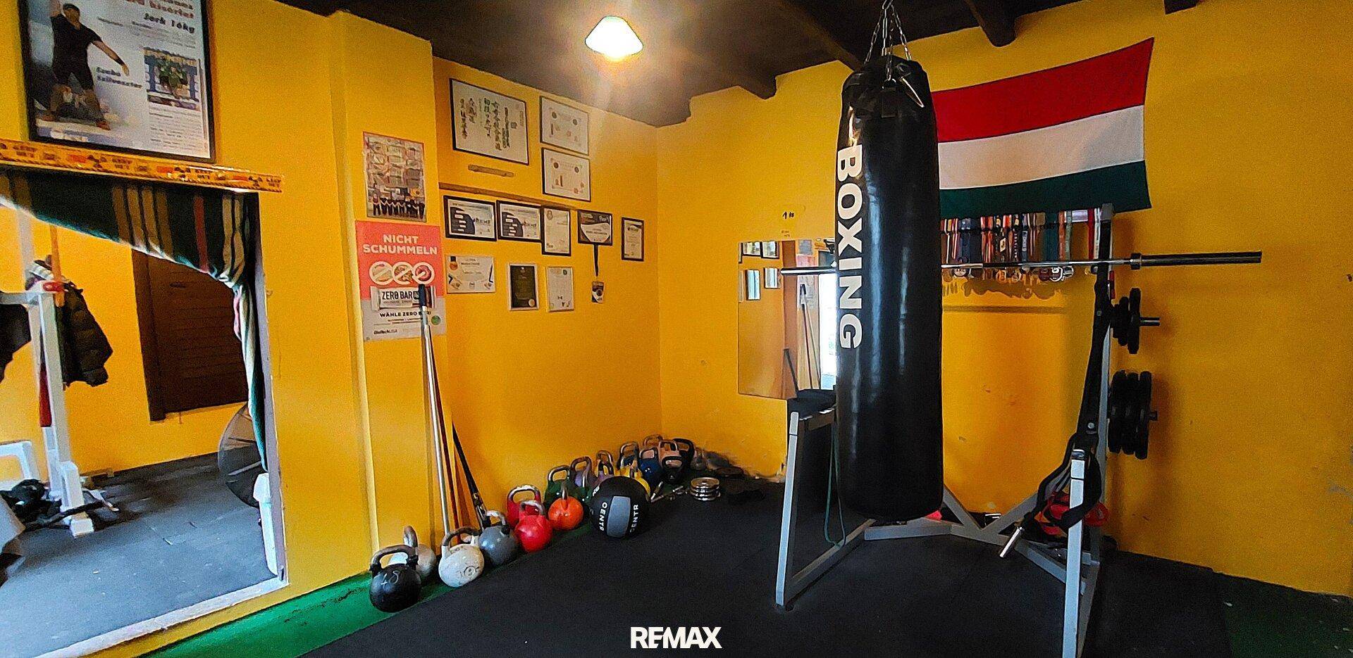 Fitnessraum mit Boxsack, Kettlebells und weiteren Trainingsgeräten in gelber Umgebung.