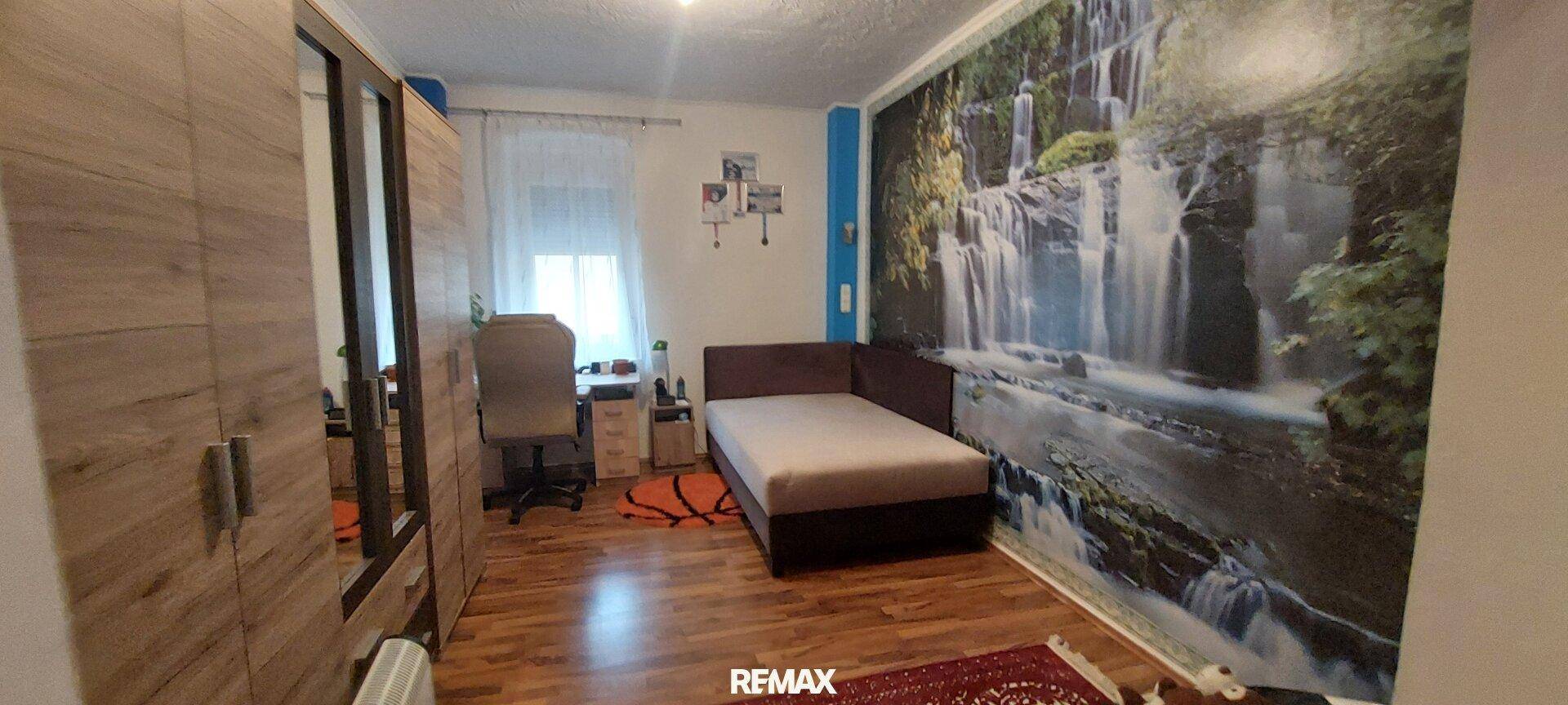 Jugendzimmer mit Bett, Schreibtisch und einer großen Wandtapete mit Wasserfallmotiv.