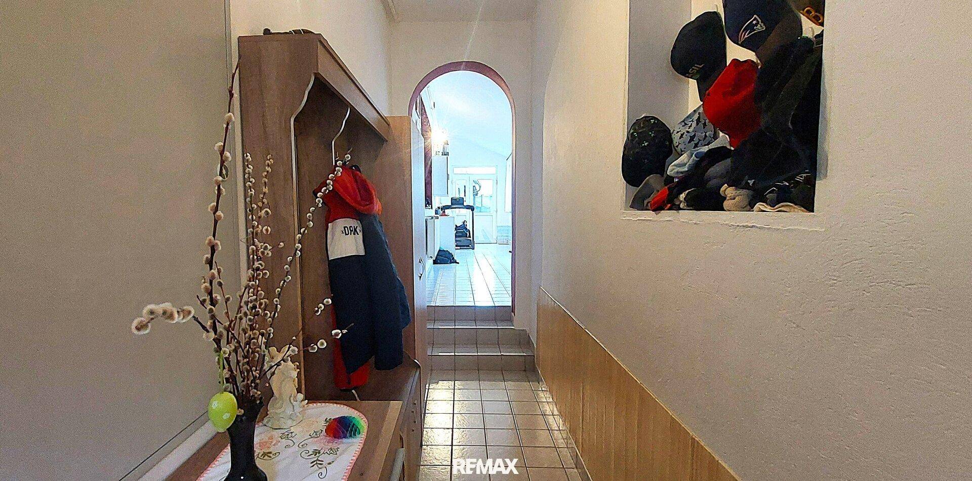 Schmaler Flur mit Garderobe, Fliesenboden und einem Durchgang zu weiteren Räumen.