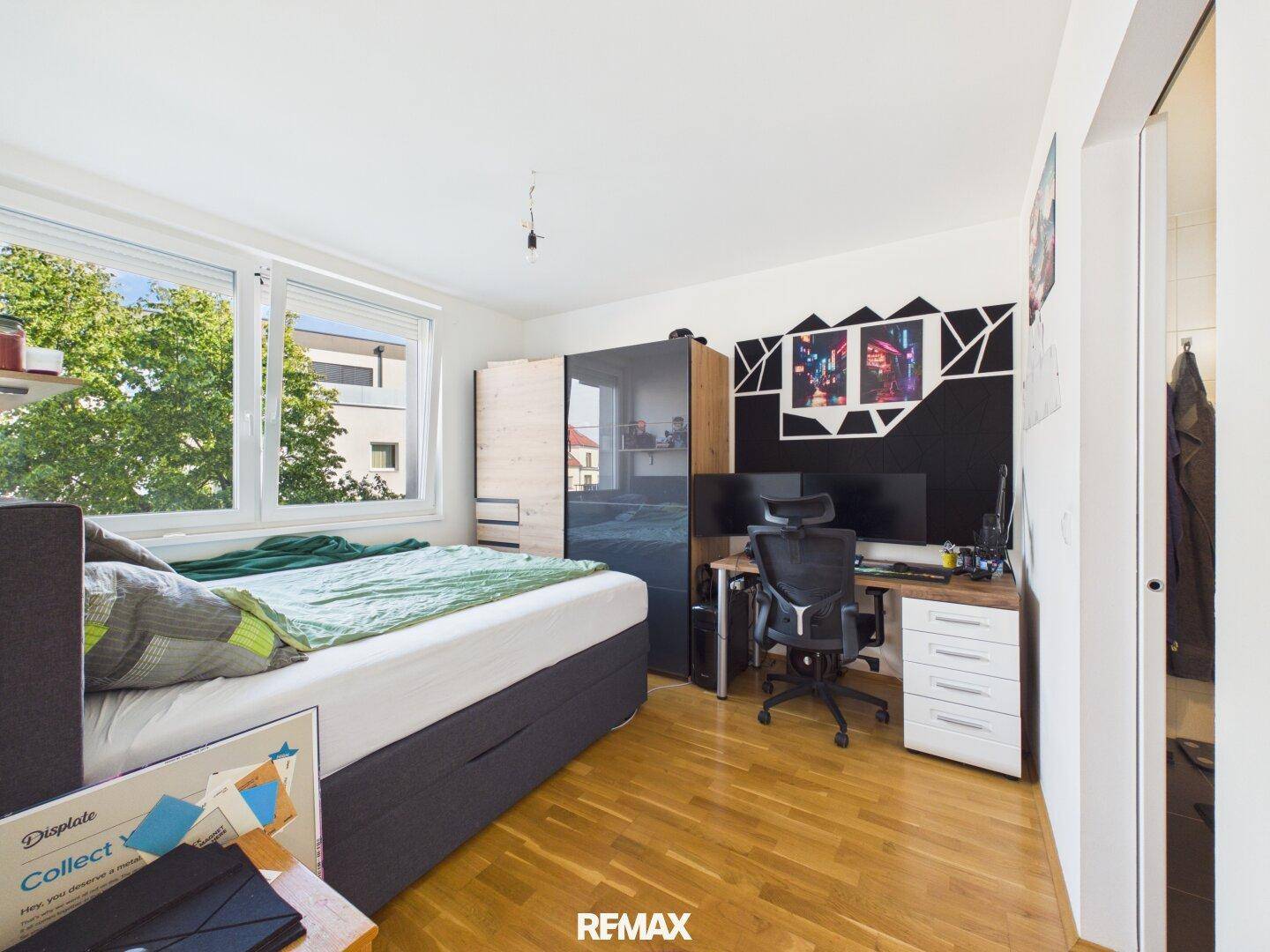 Schlafzimmer mit Holzboden, großem Fenster und Arbeitsbereich.